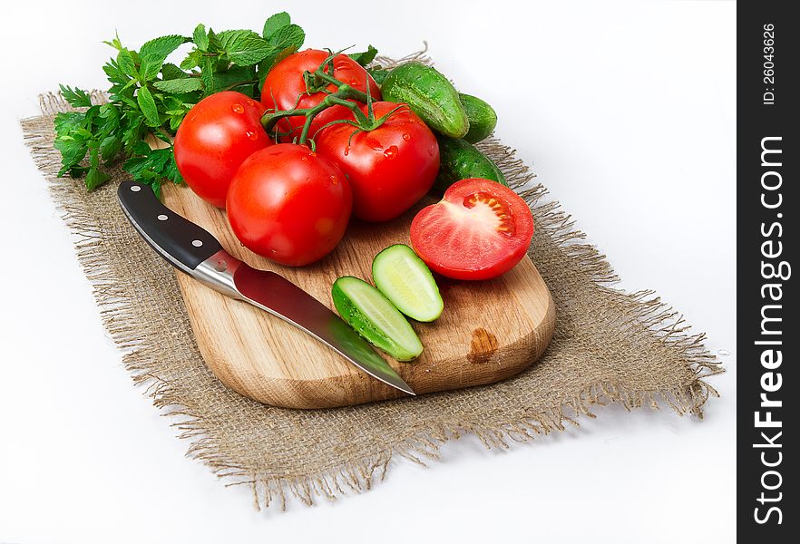 Tomatoes and cucumbers with knife on the board closeup on a white background. macro. Tomatoes and cucumbers with knife on the board closeup on a white background. macro