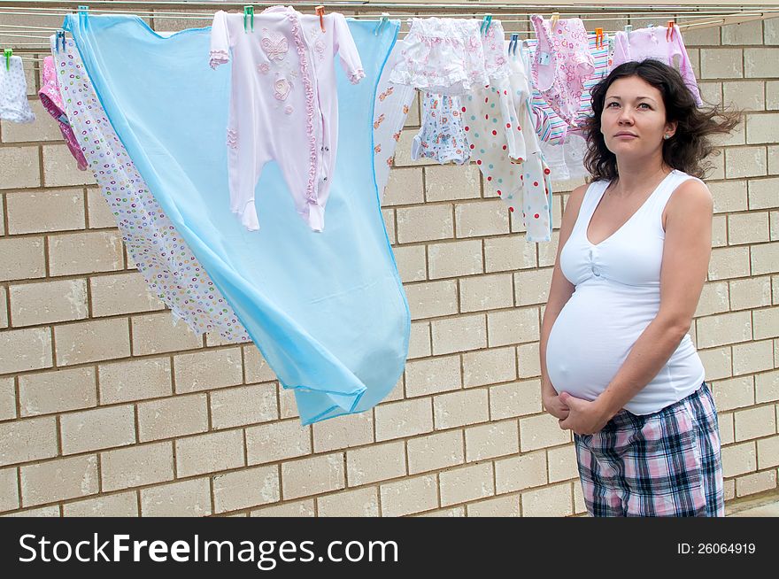 Pregnant woman looking at baby cloths on the line. Pregnant woman looking at baby cloths on the line
