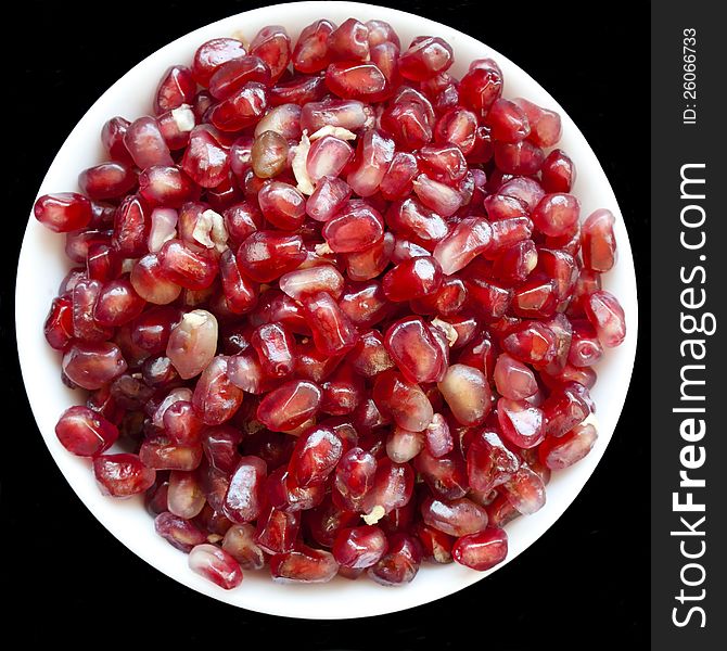 Red grains of pomegranate on white plate over black background