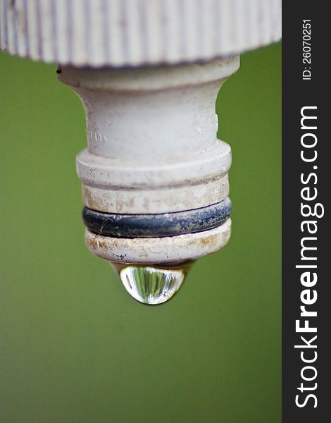 End of a spigot with water drop on it over green background. End of a spigot with water drop on it over green background