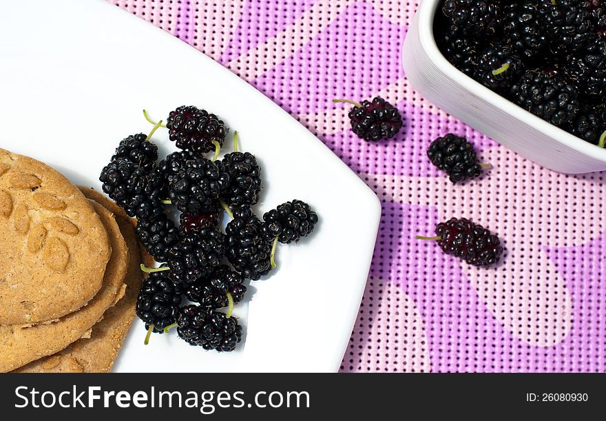 Mulberry and black currant with biscuits on a white plate on a purple table cloth. Mulberry and black currant with biscuits on a white plate on a purple table cloth