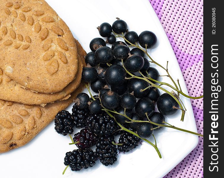 Black currant, mulberry and cereal biscuits on a white plate on a purple table cloth. Black currant, mulberry and cereal biscuits on a white plate on a purple table cloth