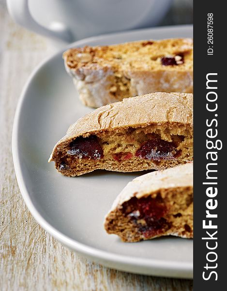 Three slices of almond biscotti biscuits with jam on the plate with a cup in the background