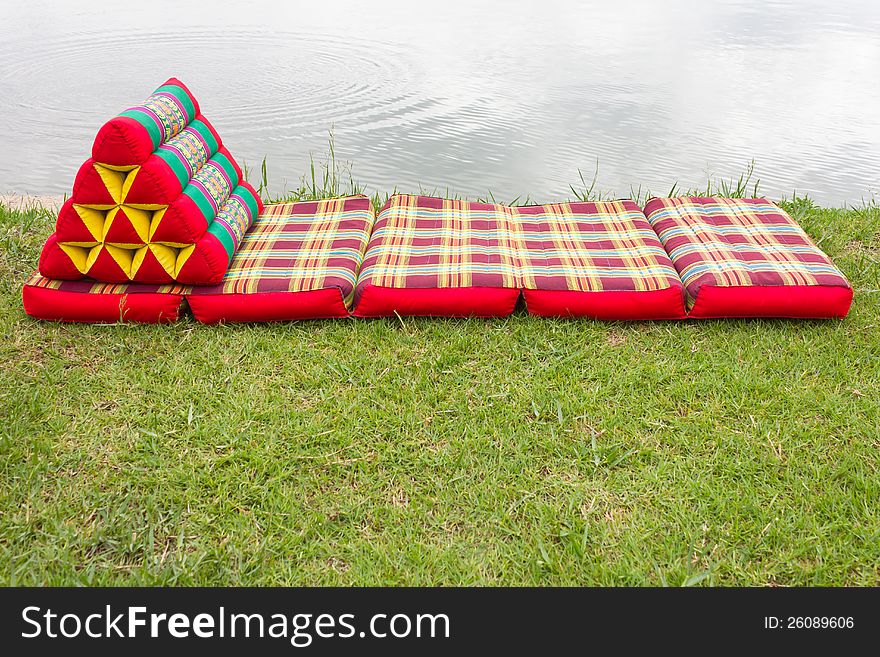 Triangular pillows and mattresses are placed on a beautiful pattern on the grass beside the pond. Triangular pillows and mattresses are placed on a beautiful pattern on the grass beside the pond.