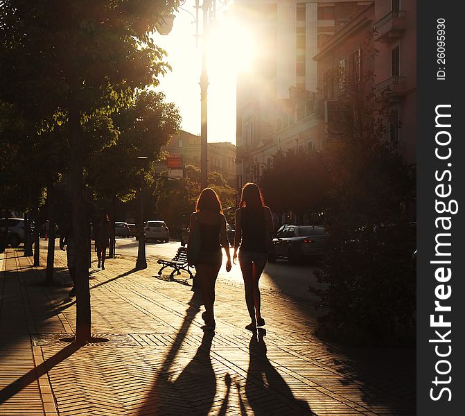 Two women walking in the sun ray, in the city.