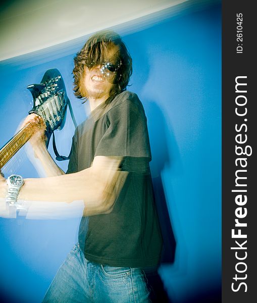 Young man smashing electric guitar over blue background, zoom and strobe lighting. Young man smashing electric guitar over blue background, zoom and strobe lighting.