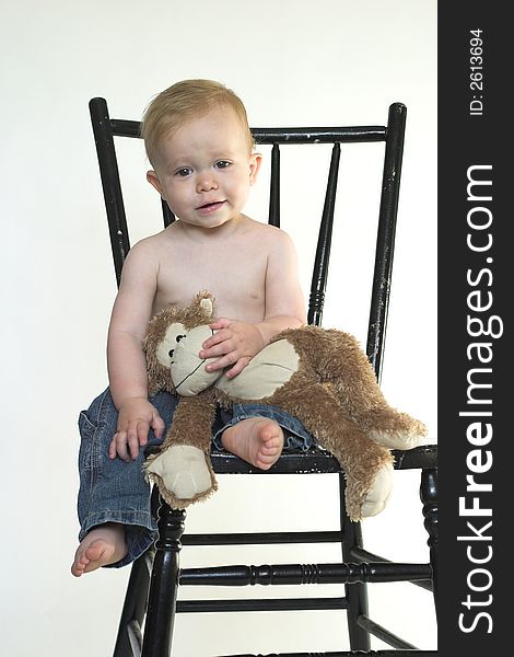 Image of a cute toddler sitting on a black chair, holding a stuffed monkey. Image of a cute toddler sitting on a black chair, holding a stuffed monkey