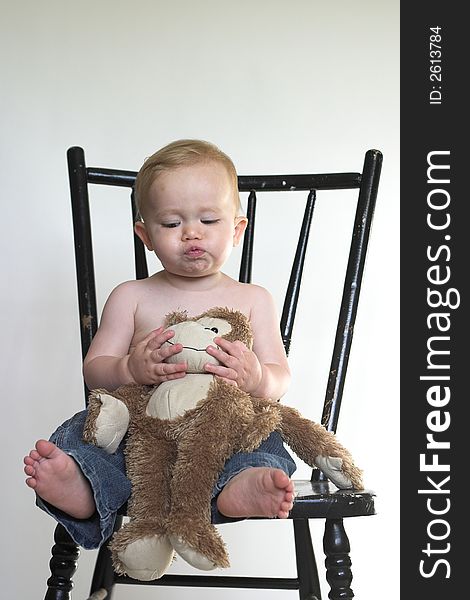 Image of a cute toddler sitting on a black chair, holding a stuffed monkey. Image of a cute toddler sitting on a black chair, holding a stuffed monkey