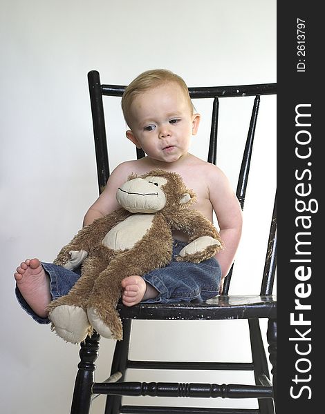 Image of a cute toddler sitting on a black chair, holding a stuffed monkey. Image of a cute toddler sitting on a black chair, holding a stuffed monkey