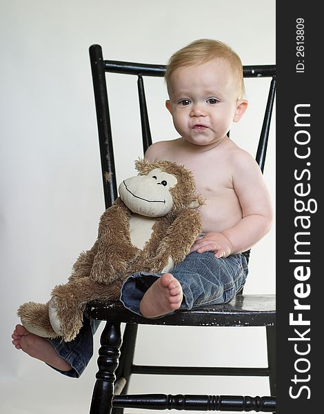 Image of a cute toddler sitting on a black chair, holding a stuffed monkey. Image of a cute toddler sitting on a black chair, holding a stuffed monkey