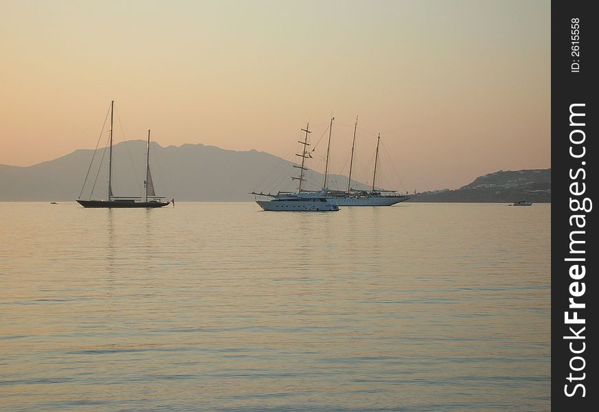A view of boats/yachts in the Mediterranean island Mykonos during sunset. A view of boats/yachts in the Mediterranean island Mykonos during sunset.