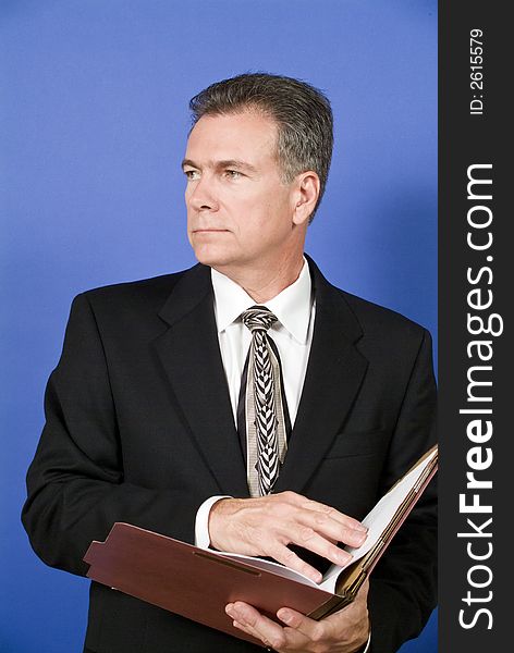 A businessman, standing in front of a blue screen, reviewing or conducting a briefing on the contents of the folder. A businessman, standing in front of a blue screen, reviewing or conducting a briefing on the contents of the folder.