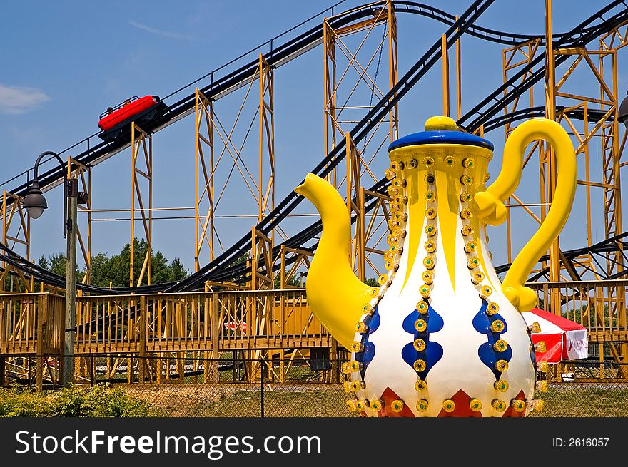 A view of a tea cup ride and a roller coaster ride at an amusement park. A view of a tea cup ride and a roller coaster ride at an amusement park.