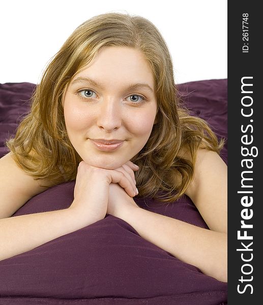 Young, beautiful woman lying in bed on violet coverlet. Smiling, looking at camera. White background. Young, beautiful woman lying in bed on violet coverlet. Smiling, looking at camera. White background