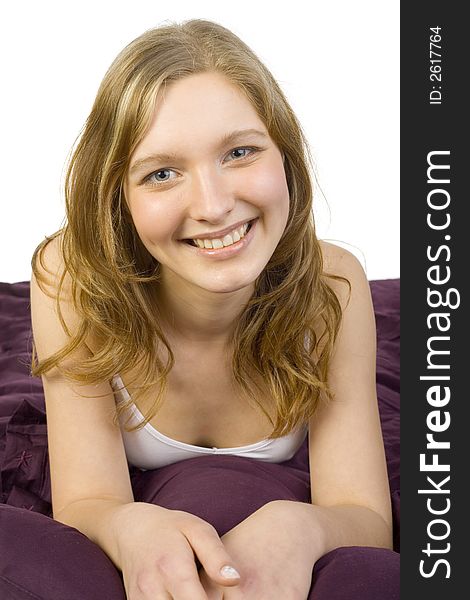 Young, beautiful woman lying in bed on violet coverlet. Smiling, looking at camera. White background. Young, beautiful woman lying in bed on violet coverlet. Smiling, looking at camera. White background