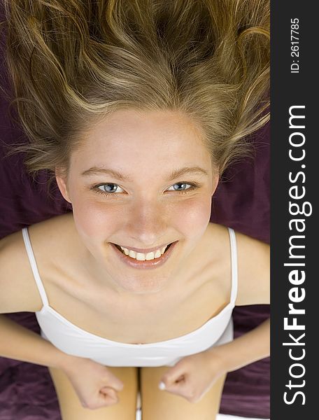 Young, beautiful woman lying in bed on violet coverlet. Smiling, looking at camera. Young, beautiful woman lying in bed on violet coverlet. Smiling, looking at camera