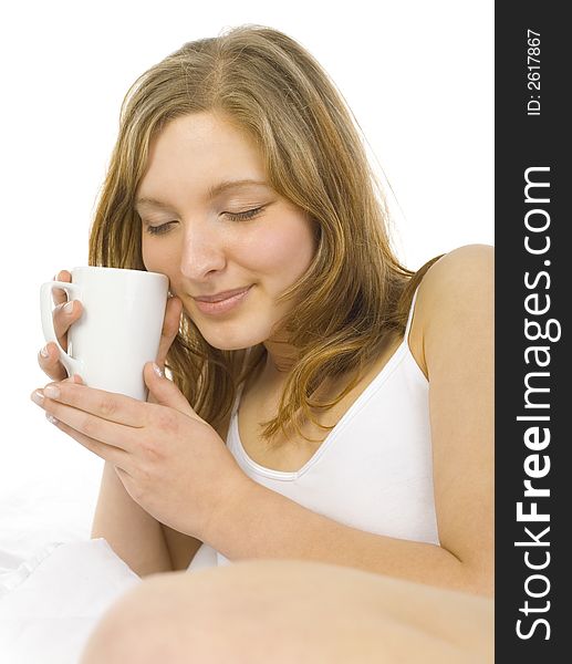 Young, beautiful woman lying in bed. Smiling and holding a cup. Closed eyes. White background. Young, beautiful woman lying in bed. Smiling and holding a cup. Closed eyes. White background