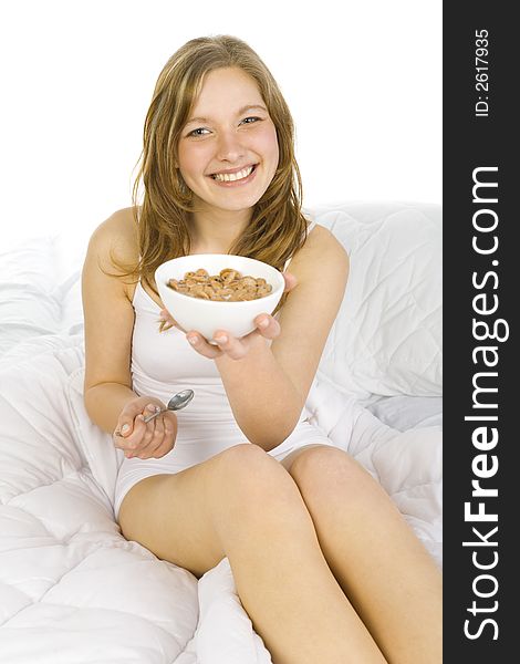 Young, beautiful woman sitting in bed. Holding a bowl of cornflakes. Offering breakfast. Looking at camera. White background. Young, beautiful woman sitting in bed. Holding a bowl of cornflakes. Offering breakfast. Looking at camera. White background