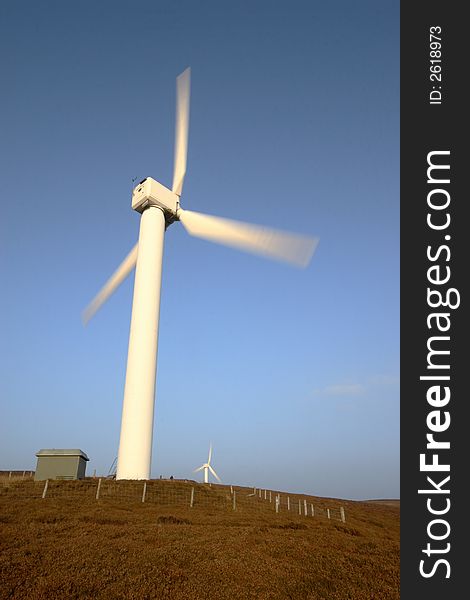Wind turbine on top of a hill. Blades of the turbine are blurred to show movement. Wind turbine on top of a hill. Blades of the turbine are blurred to show movement.