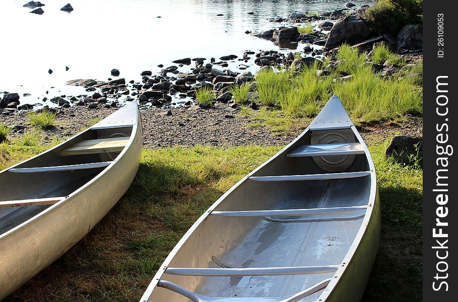 A duo of canoes, set at the edge of the lake and waiting to get out on the water again. A duo of canoes, set at the edge of the lake and waiting to get out on the water again.