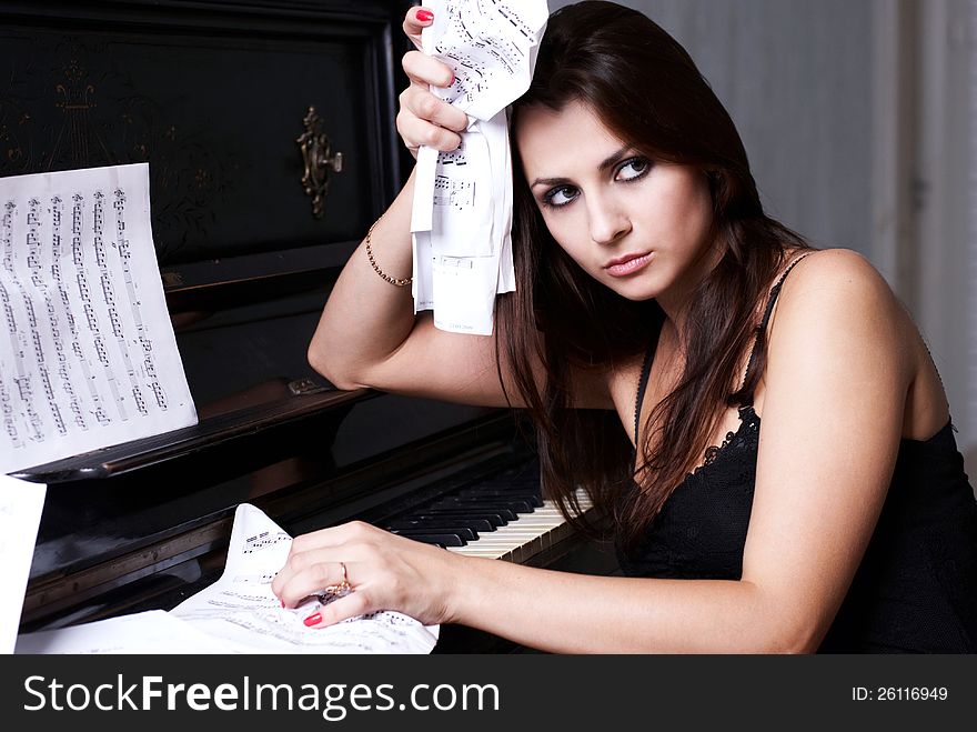 Sad girl near piano with crumpled paper with music notes everywhere