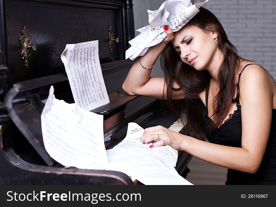 Sad girl near piano with crumpled paper with music notes everywhere