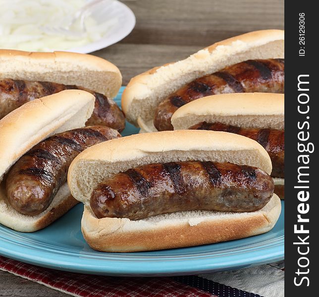 Platter of grilled bratwursts on buns with onions in background