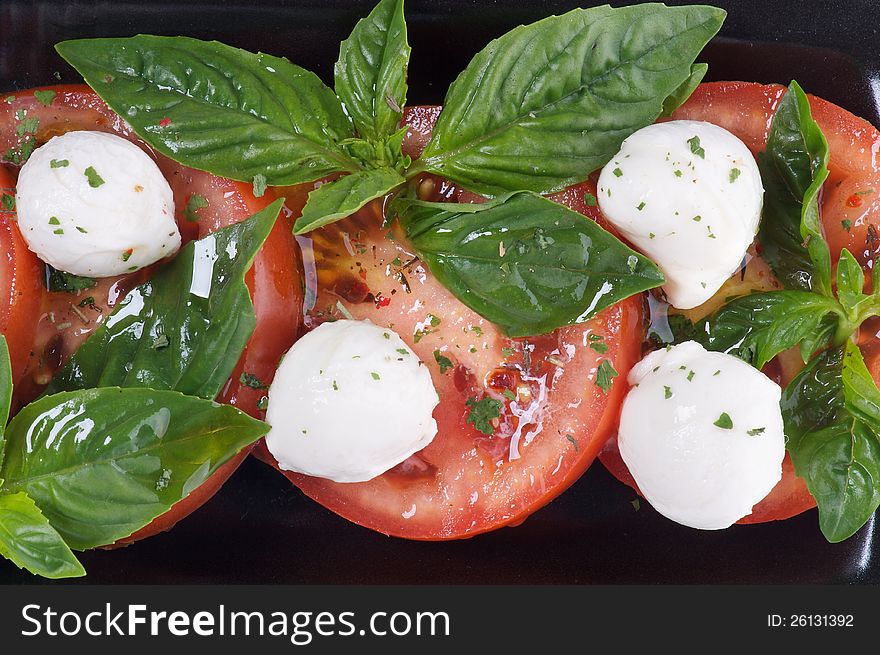 Italian Caprese Salad with Basil, Fresh Mozzarella, Tomatoes and Olive Oil on black plate close up