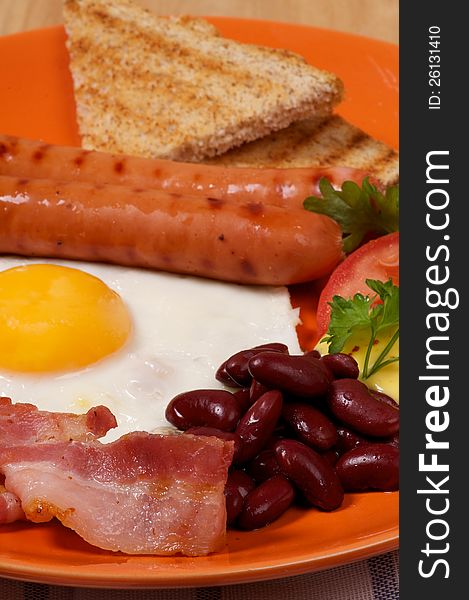 English Breakfast with Sausage, Bacon, Fried Eggs Sunny Side up, Beans, Tomato and Toasts close up on orange plate