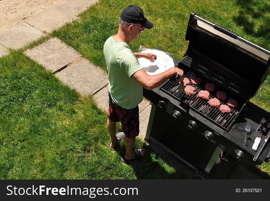 A man is cooking burgers in his backyard. A man is cooking burgers in his backyard