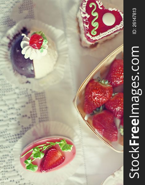 Strawberry cake in the shape of a heart,  near a basket of strawberries and another cake