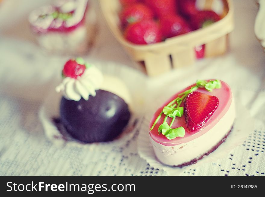 Strawberry cake in the shape of a heart,  near a basket of strawberries and another cake