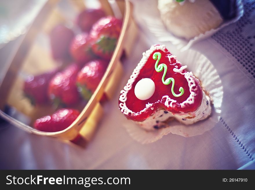 Strawberry cake in the shape of a heart,  near a basket of strawberries and another cake