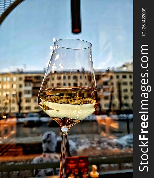 A Glass Of White Wine In Front Of A Window From A Restaurant Overlooking The City