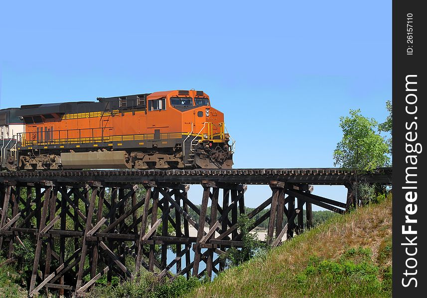 Railroad train locomotive crossing an old wooden trestle over a prairie coulee. Background of blue sky. Railroad train locomotive crossing an old wooden trestle over a prairie coulee. Background of blue sky.