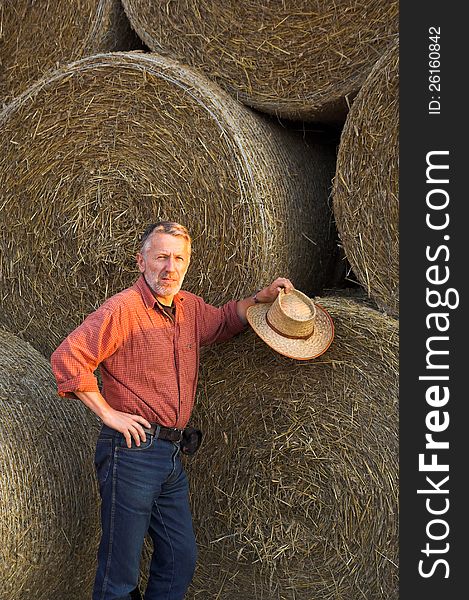 Vertical image of a farmer standing close to bales of straw in the last evening sunshine. Vertical image of a farmer standing close to bales of straw in the last evening sunshine.