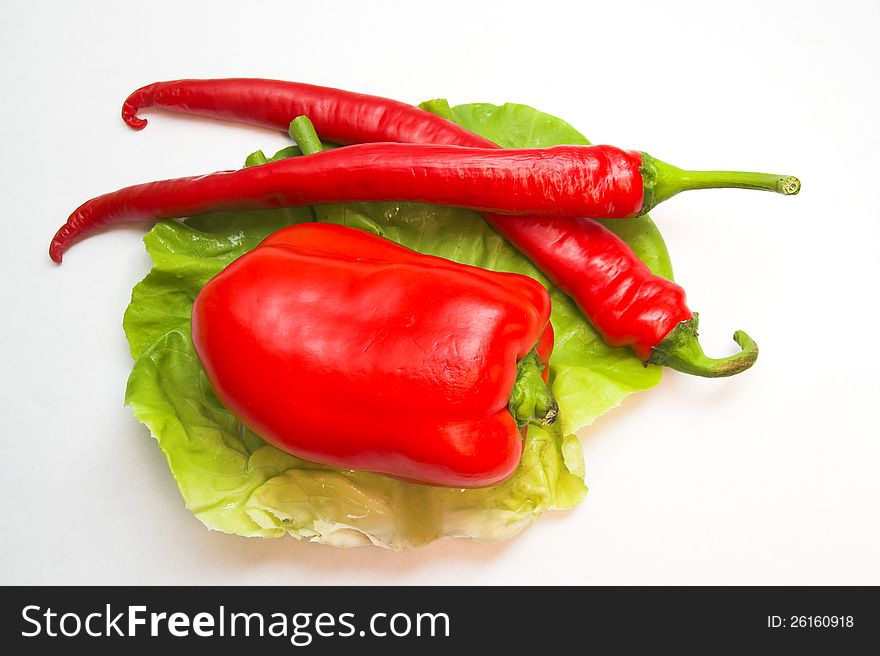 Horizontal image of  red pepper and two chilli peppers placed on a green leaf of lettuce. Horizontal image of  red pepper and two chilli peppers placed on a green leaf of lettuce