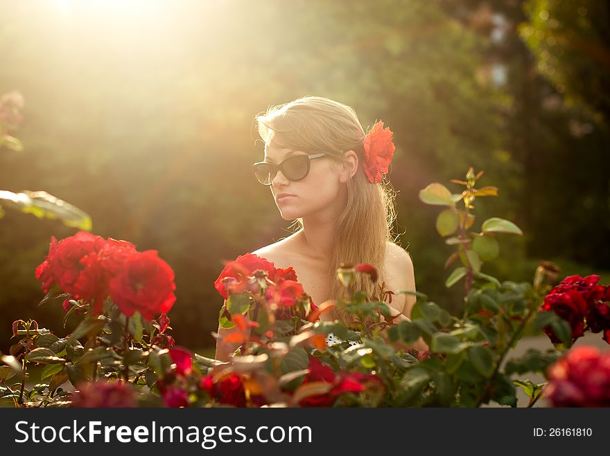 Young woman in flower garden smelling red roses 1