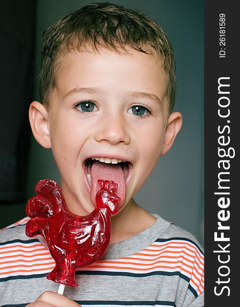 A toddler boy licks red rooster-shaped candy. A toddler boy licks red rooster-shaped candy