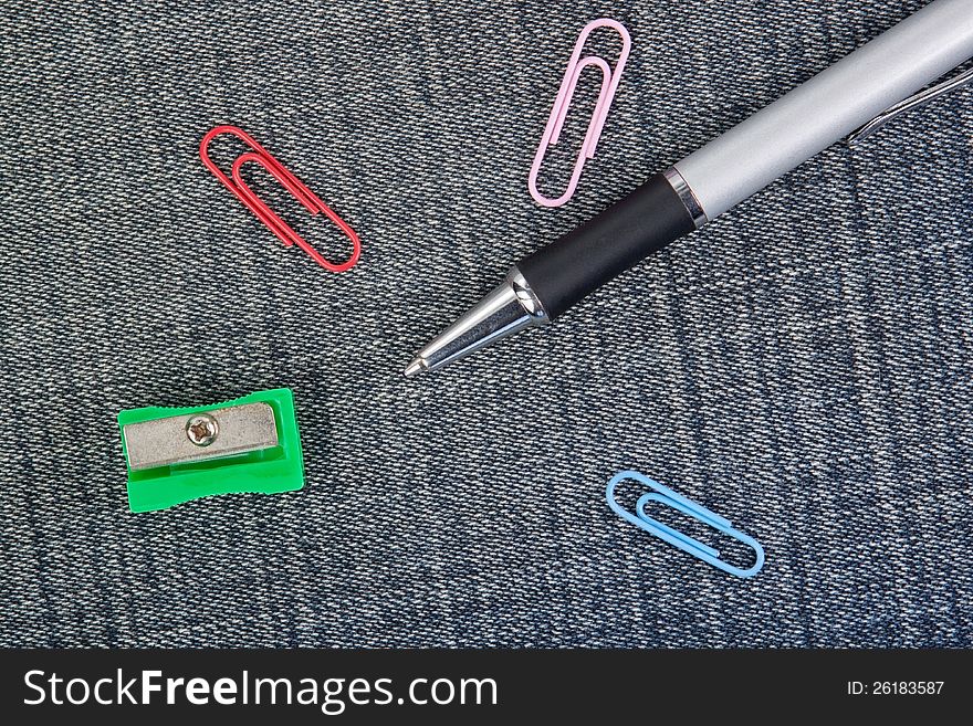 Pen, pencil sharpener and clip close-up on the background of denim material. Pen, pencil sharpener and clip close-up on the background of denim material.