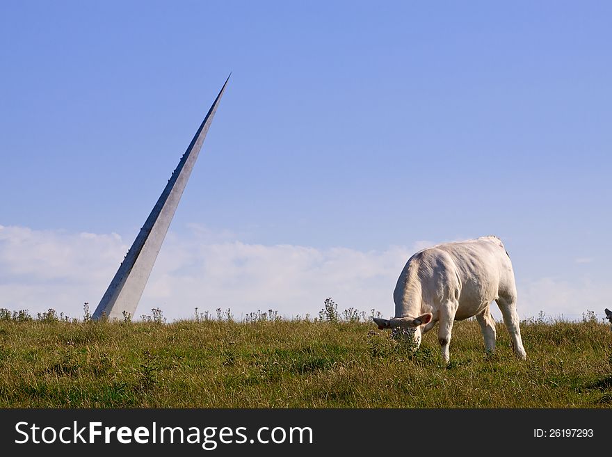 White cow eating grass in front of a sculpture of a peak. White cow eating grass in front of a sculpture of a peak