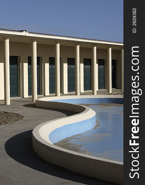 Famous beachhouse of the moviestars in Deauville,France. With a beautifull curve of the empty swimming pool in the front, arcade with green doors in the back at a sunny day. Famous beachhouse of the moviestars in Deauville,France. With a beautifull curve of the empty swimming pool in the front, arcade with green doors in the back at a sunny day.