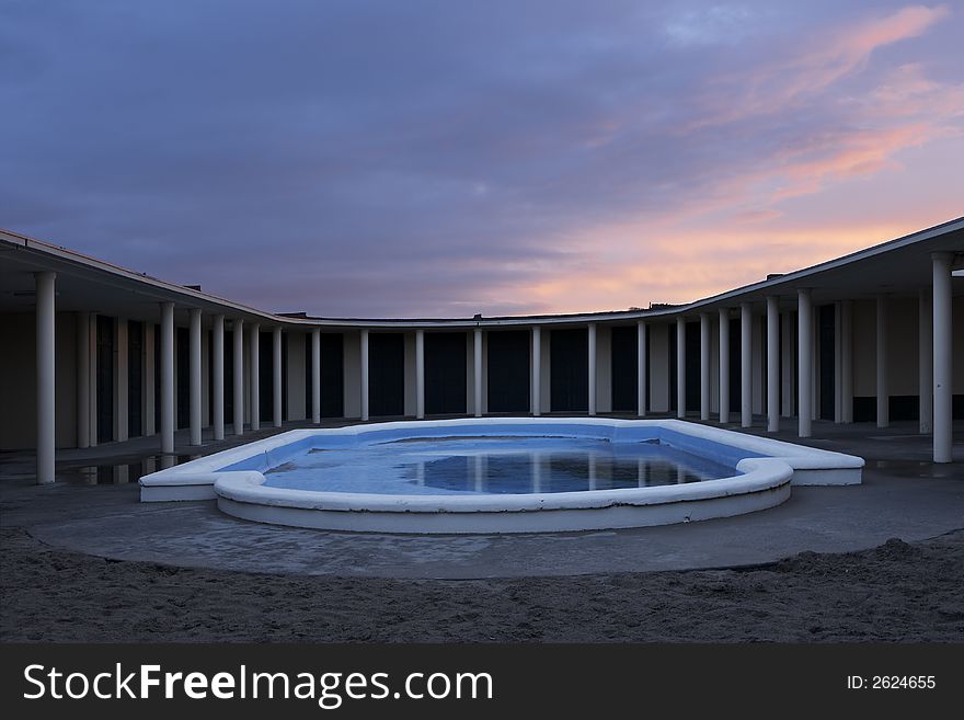 Early morning at Deauville bathouse of the moviestars. The swimming pool in a symmetrical photo with just a bit of water in it and a red sunrise above the colonades. Early morning at Deauville bathouse of the moviestars. The swimming pool in a symmetrical photo with just a bit of water in it and a red sunrise above the colonades.