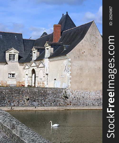 The old stables at Château Plessis-Bourré and a Swan swimming in the moat, France, Europe. The old stables at Château Plessis-Bourré and a Swan swimming in the moat, France, Europe