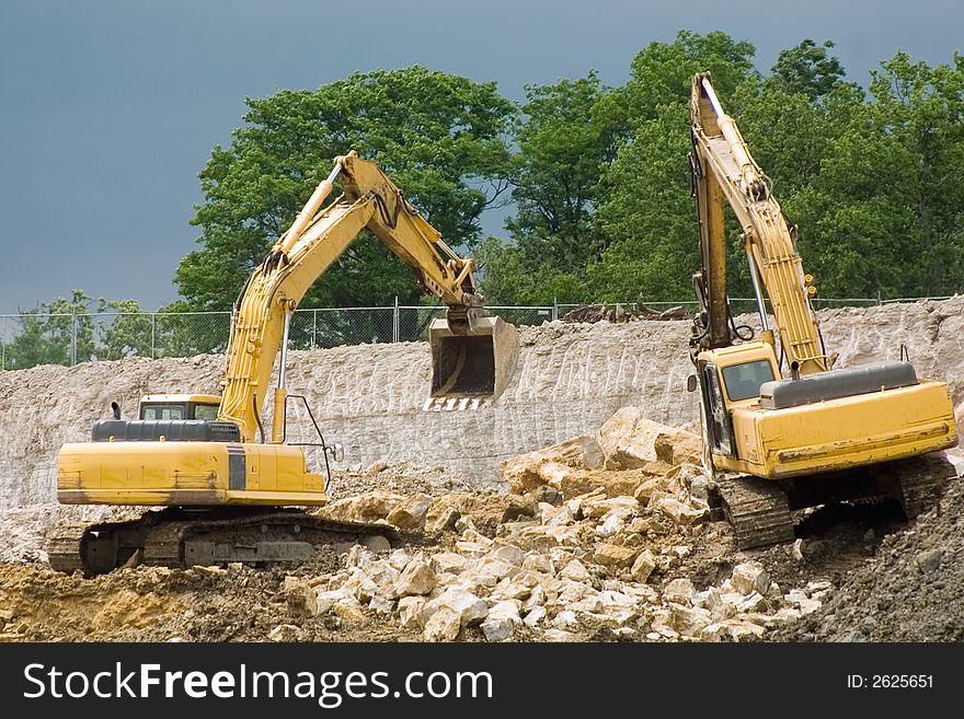 Picture of two backhoes moving dirt and large rocks at a construction site. Picture of two backhoes moving dirt and large rocks at a construction site.