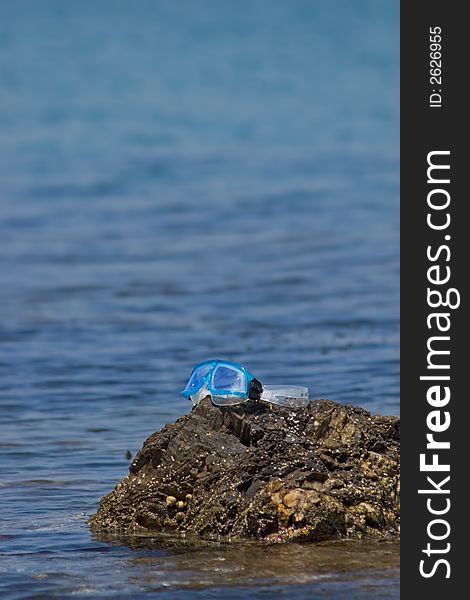 Diving mask posed on a rock at the edge of the sea