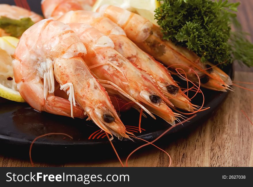 LArge shrimps cooked in shell served on a plate with lemon and greens - closeup