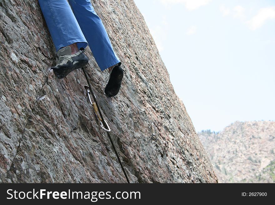 A rock climbers legs and shoes are holding you on the rock. A rock climbers legs and shoes are holding you on the rock