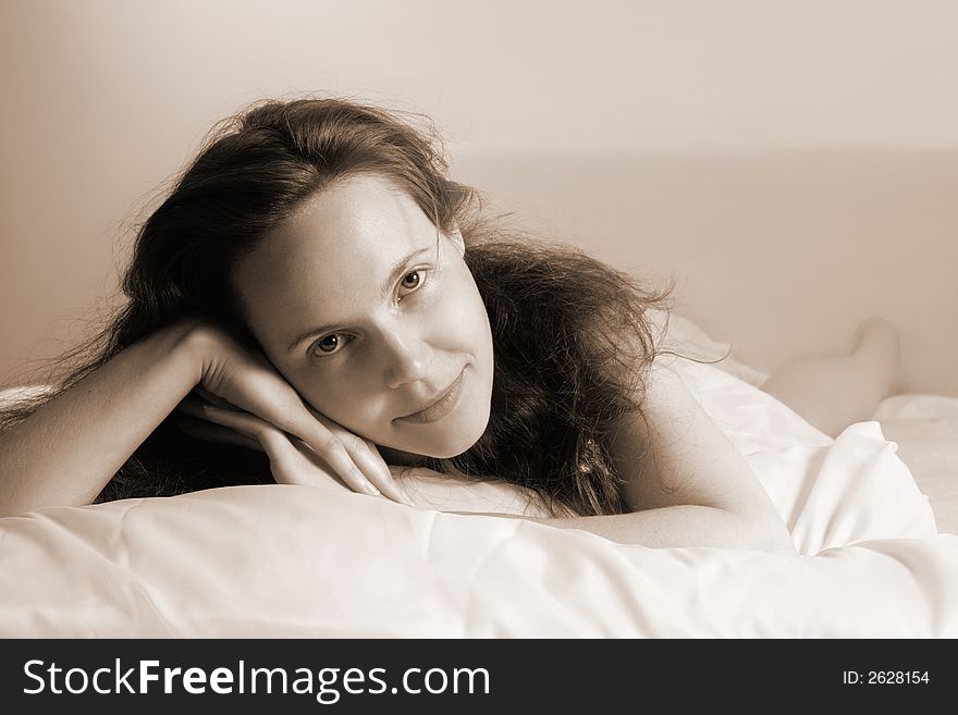 Portrait of a young awakened smiling woman lying on a bed(soft-focused+sepia toned). Portrait of a young awakened smiling woman lying on a bed(soft-focused+sepia toned)