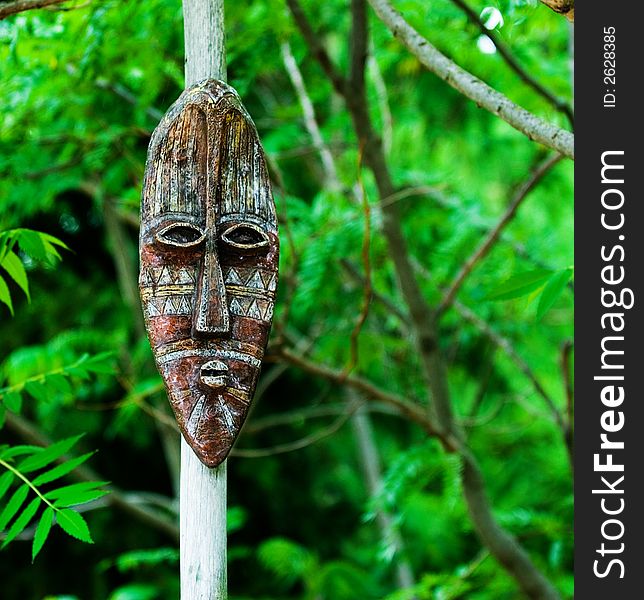 A Tribal mask mounted on a wooden pole with forest background. A Tribal mask mounted on a wooden pole with forest background